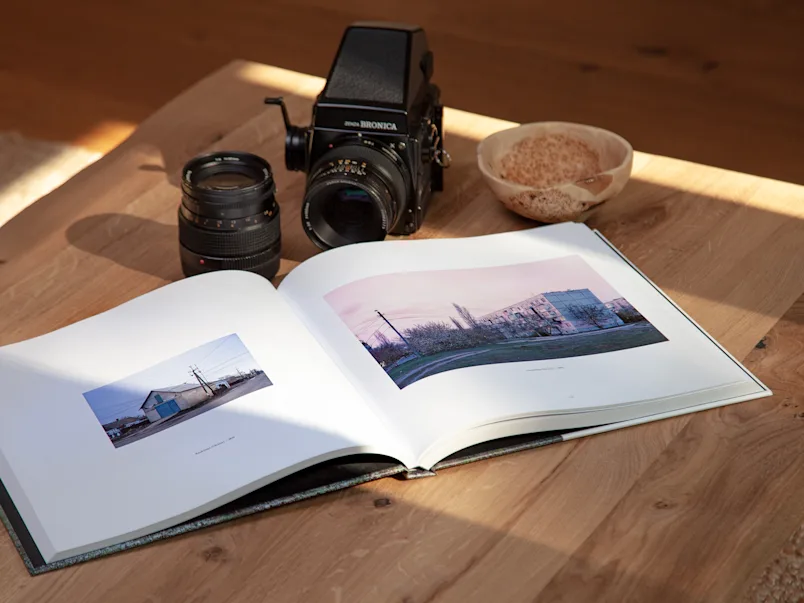 PDP | Bildband | Product Selector Section (US, BE, IT, ES, EU) | Media #3 | Image An open coffee table book lying on a table with a camera next to it