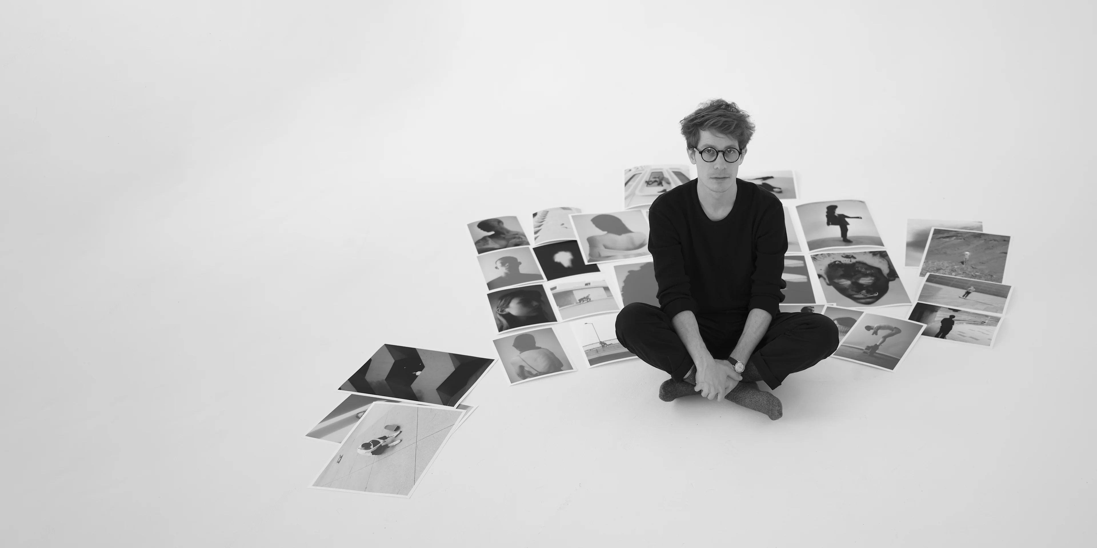 Image of photographer Alexandre Souêtre sitting on the floor with his printed photographs around him.